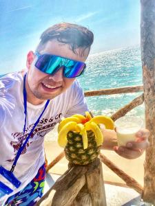 a man wearing sunglasses holding a pineapple and a drink at Hostal Playa Blanca in Playa Blanca