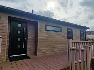 una casa con terrazza in legno con porta nera di Derwen 2 Bedroom Luxury Lodge a Welshpool