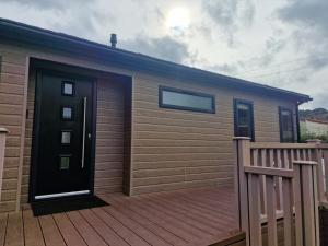 a house with a wooden deck with a black door at Derwen 2 Bedroom Luxury Lodge in Welshpool