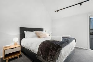 a white bedroom with a large bed and a night stand at Nestled below the Remarkables in Queenstown