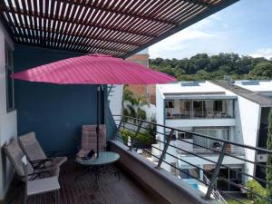 Un balcón con una sombrilla rosa, sillas y una mesa. en Condominio Terrazas del Sol, en Sopetrán