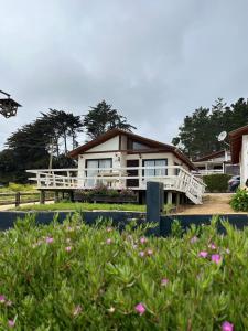 a house with a porch and flowers in front of it at Cabañas Lomas de Pinares in Pichilemu