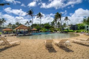 a pool at a resort with chairs and palm trees at Kauai Beach Resort #1317 in Lihue