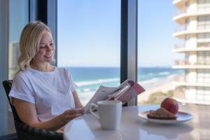 a woman sitting at a table reading a book at Meriton Suites Surfers Paradise in Gold Coast
