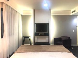 um quarto com uma cama, uma televisão e uma cadeira em Apto Privativo em Hotel de Luxo no Ibirapuera em São Paulo