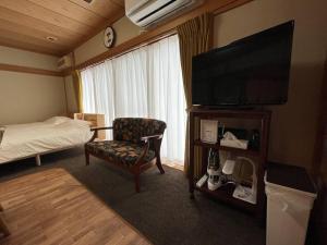 Pokój hotelowy z telewizorem, łóżkiem i krzesłem w obiekcie 草津温泉 湯之風 w mieście Kusatsu