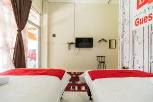 two beds in a room with a tv on the wall at RedDoorz Syariah near Pasar Aur Kuning in Bukittinggi