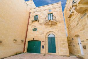 a building with two green doors and a balcony at Rebbiegha Holiday Home in Qala