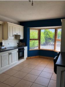 a kitchen with blue walls and white cabinets and windows at Picturesque Riverside Home in Cahersiveen