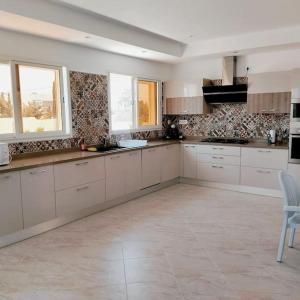 duża kuchnia z białymi szafkami i oknami w obiekcie Magnifique villa avec piscine w mieście Djerba