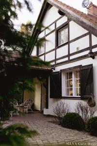 ein weißes Haus mit schwarzen Fenstern und einer Terrasse in der Unterkunft SILVA Guest House - dom wczasowy, tenis, basen, balia i sauna in Borsk