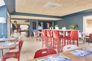 une salle à manger avec des tables et des chaises rouges dans un restaurant dans l'établissement Kyriad Caen Nord - Hérouville-Saint-Clair, à Hérouville-Saint-Clair