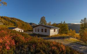 a small white building on a hill with trees and mountains at Bungalow in Sirdal in Tjørhom