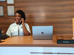 een vrouw die aan een bureau met een laptop met een mobiele telefoon praat bij KoKo Palm Inn in Accra