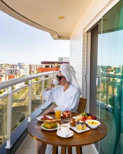 una mujer sentada en una mesa con comida en un balcón en Oasis Cabo Frio, en Cabo Frío