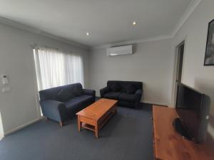 sala de estar con 2 sillas, mesa y TV en Belvoir Village Motel & Apartments Wodonga, en Wodonga