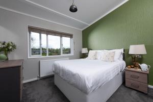 ein Schlafzimmer mit einem weißen Bett und einer grünen Wand in der Unterkunft Daisy Lodge, 6 Roadford Lake Lodges in Lifton