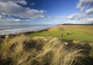 two people standing on a golf course next to the ocean at Ty’n Fron in Penegoes