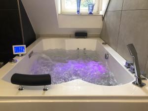 Bed and Breakfast De Haen - Privé-appartementen van 43 of 60 m2 met tweepersoons bubbelbad - Finse sauna - in westvleugel van luxe villa في أوس: حوض استحمام مملوء بالماء الأرجواني في الحمام