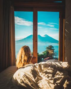 a woman laying in bed looking out a window at Lush Atitlán in San Marcos La Laguna