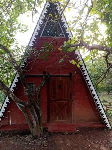 a red barn with a wooden door and a tree at Porsu in Canacona