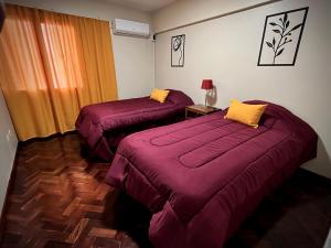 2 camas en una habitación con sábanas moradas y almohadas amarillas en El Carnaval Apart Jujuy en San Salvador de Jujuy