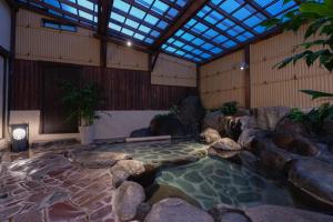 Una piscina de agua en una habitación con rocas y techo en Isoaruki no Yuyado Ushiogumo -6 years or older-, en Kawazu