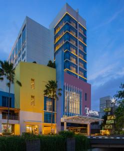 a tall building with a colorful facade and palm trees at ARTOTEL TS Suites Surabaya in Surabaya