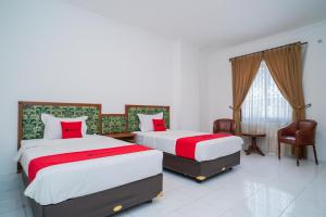 two beds in a white room with red pillows at RedDoorz Plus at Hotel Surya Solo in Solo