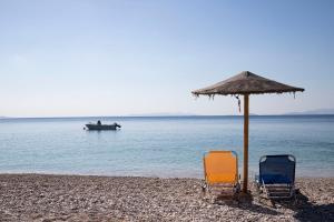 dos sillas y una sombrilla en una playa con un barco en Seaside Haven Kineta, en Kineta