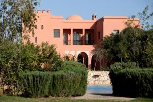 a pink house with a garden in front of it at Domaine de l'Arganeraie Essaouira in Essaouira +110 photos