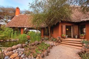 een huis met een rieten dak en een vijver aan de voorkant bij Tawi Lodge in Amboseli