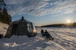 duas pessoas estão sentadas em cadeiras na neve em Aurora hut igloo em Rovaniemi