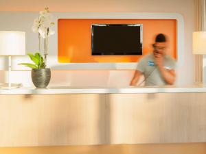 a man standing behind a counter with a television at ibis budget Antwerpen Port in Antwerp