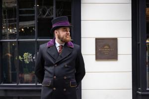 Un uomo con un cilindro davanti a un palazzo di Sun Street Hotel Shoreditch a Londra