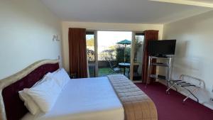 a bedroom with a bed with a television and a balcony at Chantillys Motor Lodge in Taupo