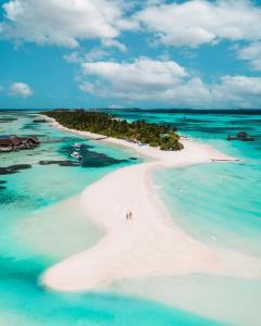 an island in the ocean with two people on a beach at LUX* South Ari Atoll Resort & Villas in Maamigili