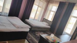 1 dormitorio con 2 camas, mesa y ventanas en Tomaris, en Nukus