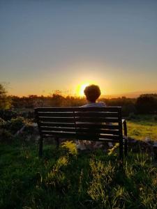 Eine Person, die auf einer Bank sitzt und den Sonnenuntergang beobachtet. in der Unterkunft A Casa do Portal in Campo Lameiro