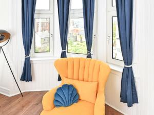 an orange chair in a room with blue curtains at John Muir Apartment in Helensburgh