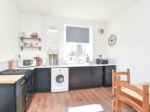 een keuken met zwarte kasten en een wasmachine en droger bij John Muir Apartment in Helensburgh