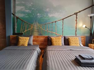 twee bedden in een kamer met een schilderij van een hangbrug bij โรงแรม บอร์ดดิ้งเฮ้าส์ in Ban Bang Yai Chuai