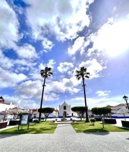 un parco con palme e un edificio bianco di Calmaria Guesthouse a Porto Covo