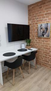 a white desk with two chairs and a tv on a brick wall at Apartamenty K&B Toruń in Toruń