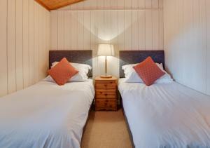 2 Einzelbetten in einem Zimmer mit einer Lampe auf einem Nachttisch in der Unterkunft Birch Lodge in Thornton Watlass