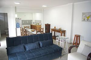 a living room with a blue couch and a kitchen at Casa com 2 quartos à 200 m da da praia c/ churrasqueira in Palhoça