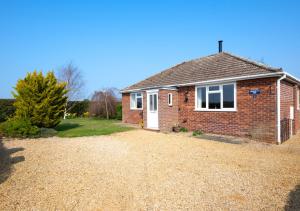 a brick house with a white door on a gravel driveway at Journeys End in Ringstead