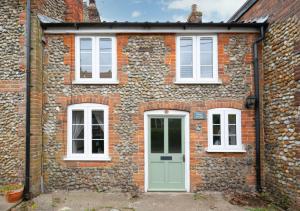 a brick house with a green door and white windows at Poppy Cottage in Briston