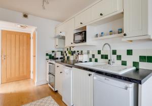 a kitchen with white cabinets and green and white tiles at Half Pint in Southwold