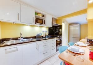 une cuisine avec des placards blancs et une table en bois dans l'établissement Shoreline, à Aldeburgh